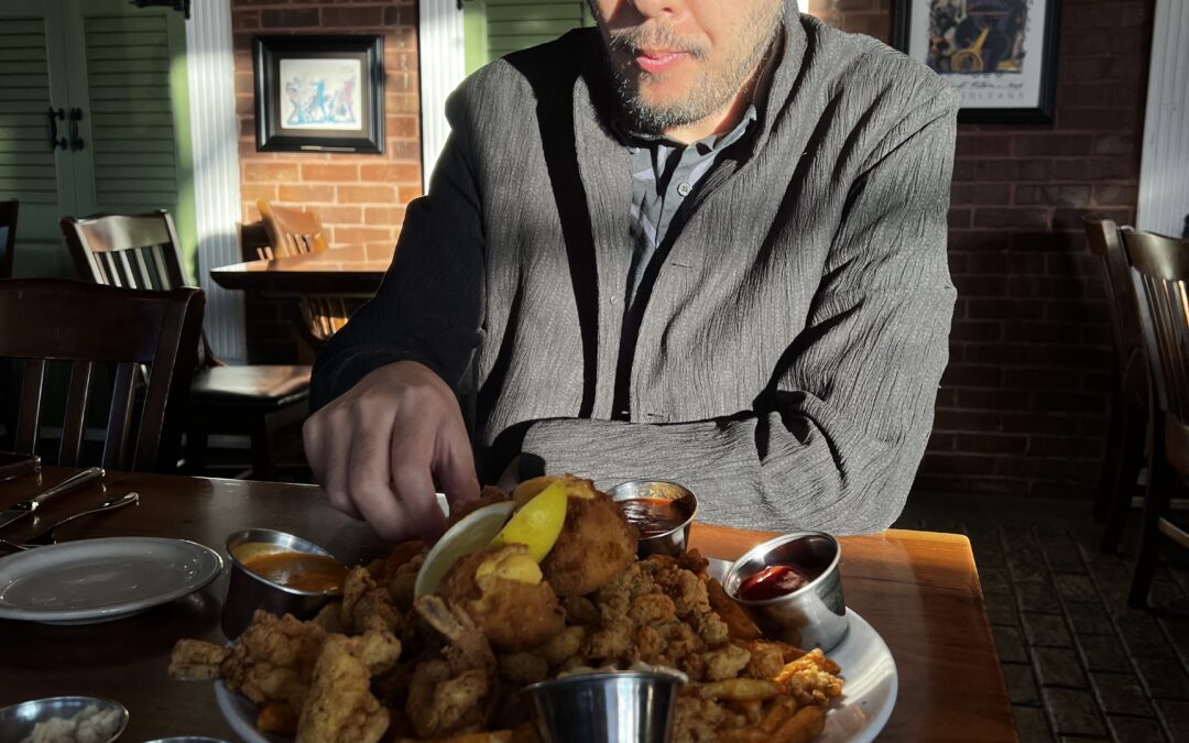 Katusya Yuasa is seated behind a large plate of fried seafood in a restaurant in Oklahoma