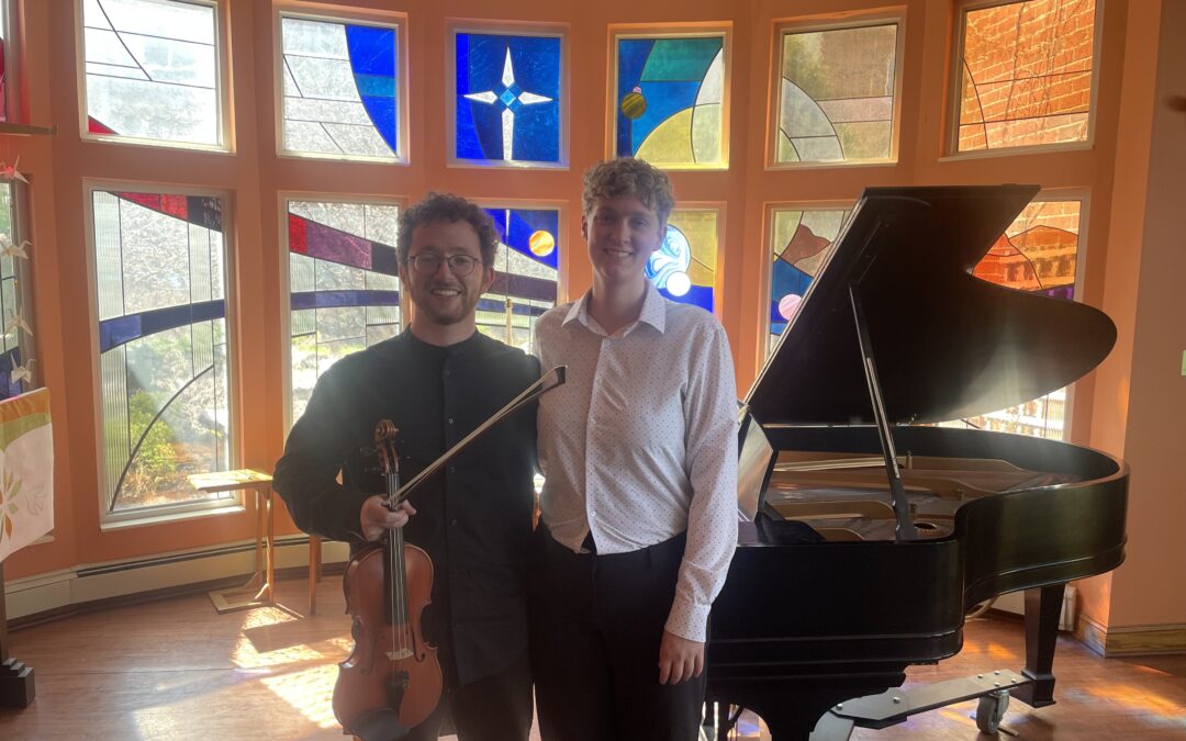 A violinist and a pianist standing in front of a baby grand piano before a concert.